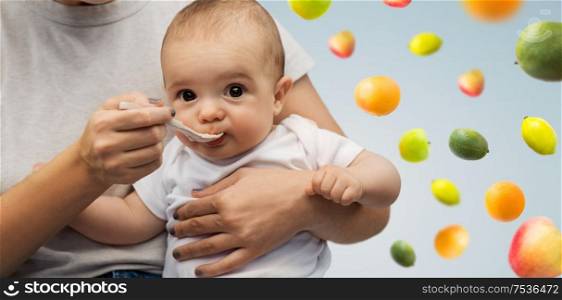 child, eating and food concept - close up of mother with spoon feeding little baby over fruits on background. close up of mother with spoon feeding little baby