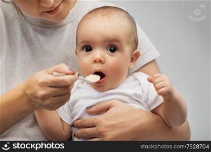 child, eating and food concept - close up of mother with spoon feeding little baby. close up of mother with spoon feeding little baby