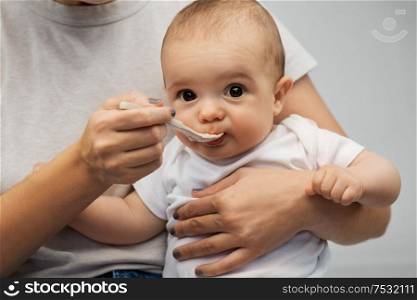 child, eating and food concept - close up of mother with spoon feeding little baby. close up of mother with spoon feeding little baby