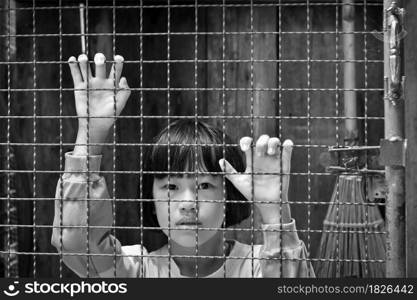 Child girl behind the fence, hand holding steel mesh, black and white toned photo.