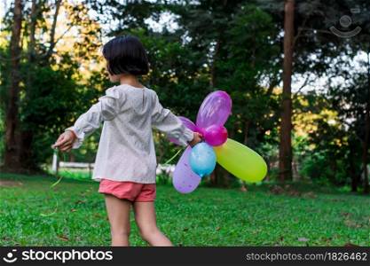 Child girl holding colorful toy balloons in the park outdoors.
