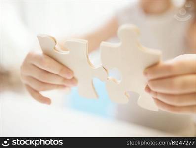 Child girl holding two big wooden puzzle pieces. Hands connecting jigsaw puzzle. Close up photo with small dof. Education and learning concept.. Child girl holding two big wooden puzzle pieces. Hands connecting jigsaw puzzle. Close up photo with small dof. Education and learning concept