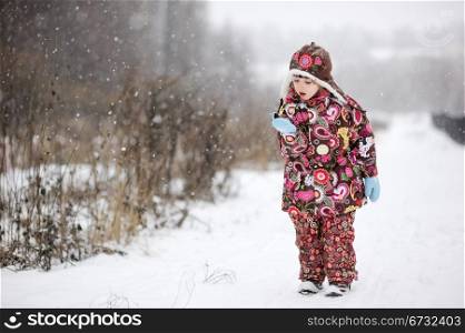 Child girl in colorful snowsuit plays outdoors in snowfall