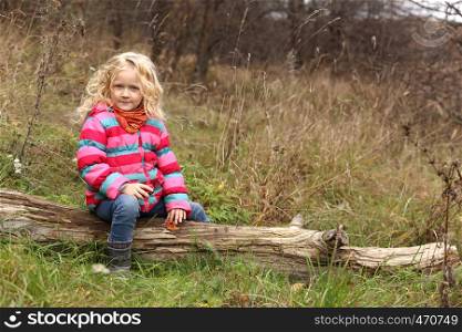 child girl sitting on a log at the autumn forest