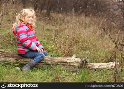 child girl sitting on a log at the autumn forest