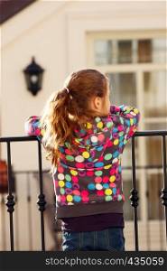 child girl standing on a balcony and looking to the street