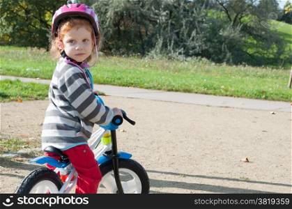 Child girl with the safety helmet on the bike in the autumn park