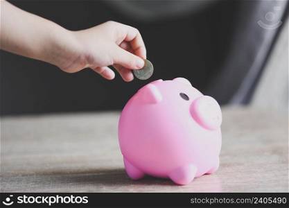 Child hand putting money coin into piggy bank for saving money for education study, Save money concept