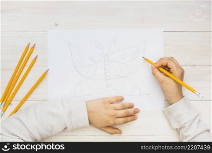 child hand sketching butterfly with pencil wooden background