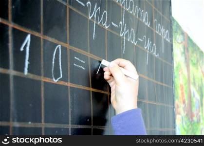 child hand writing numbers on school blackboard close up