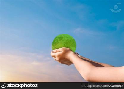 Child hands holding green earth globe over blurred sunset sky background. World environment day concept