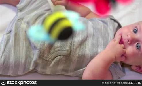 Child having fun in cradle at home, happy cute little boy laughing and playing with toy and puppets in bed. Male infant with blue eyes in baby crib