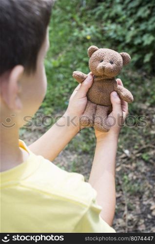 Child hold teddy in a garden.