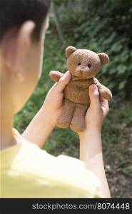 Child hold teddy in a garden.