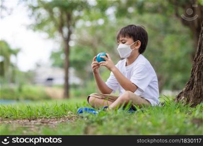 Child holding a globe with a face mask on it - Conceptual Corona virus Covid-19 virus pandemic and pollution concept.