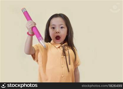 Child holding big pencil on light brown background. Shocked or surpised kid.