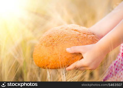 Child holding bread in hands against yellow autumn wheat background. Shallow depth of fields