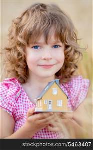 Child holding house in hands against autumn yellow background. Real estate concept