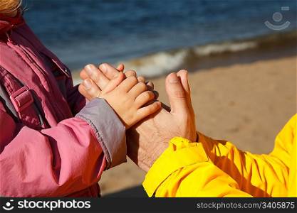 Child holds hand of adult. Photo close-up, on sunny autumn day.