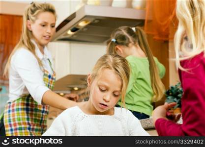 Child in a kitchen with sisters around her and her mother doing homework