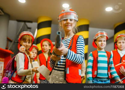 Child in helmet and uniform with hose in hands playing fireman, playroom indoor. Kids lerning firefighter profession. Children lifeguards, little heroes in equipment on playground