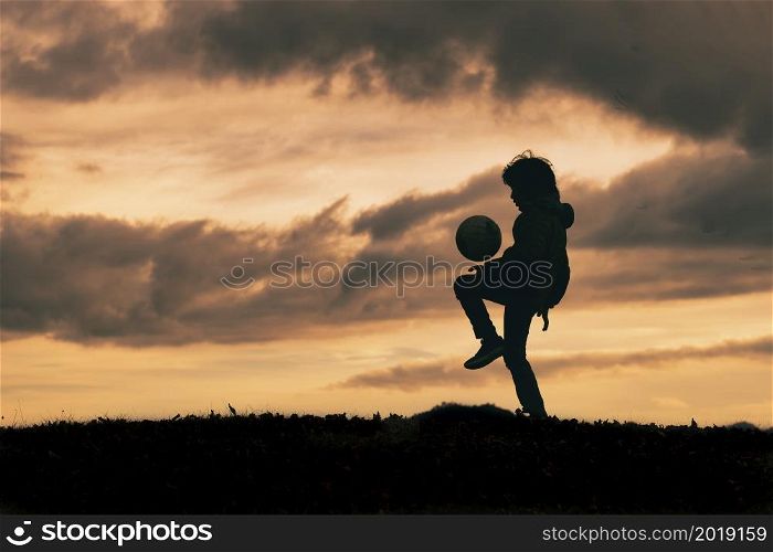 Child in silhouette dribbles and plays with soccer ball