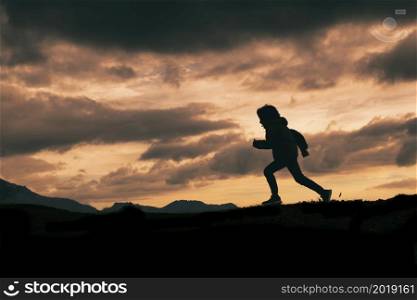 Child in silhouette while running on a meadow