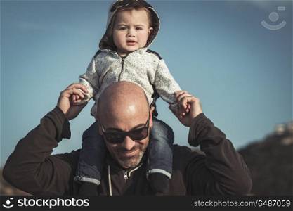 Child is sitting on his father&rsquo;s shoulders, handsome dad playing with his cute little son, enjoying parenthood, family love concept. Happy father with son