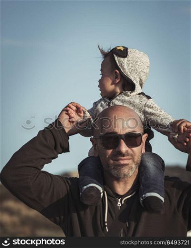 Child is sitting on his father&rsquo;s shoulders, handsome dad playing with his cute little son, enjoying parenthood, family love concept. Happy family life
