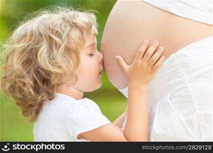 Child kissing belly of pregnant woman against spring green background