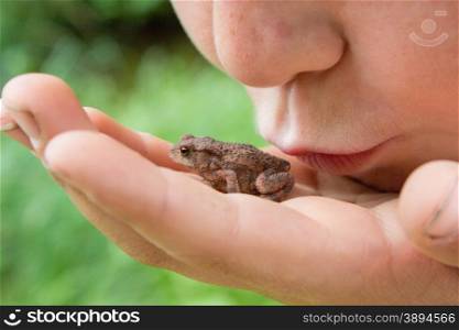Child kissing frog on his hand. Mouth close to animal