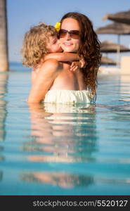 Child kissing smiling woman in swiming pool. Summer vacations concept