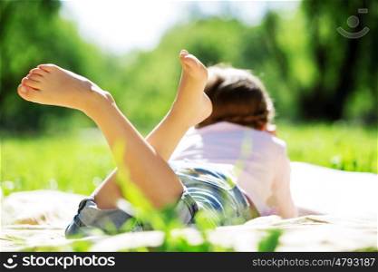 Child lying on blanket having picnic in summer park. Girl in park