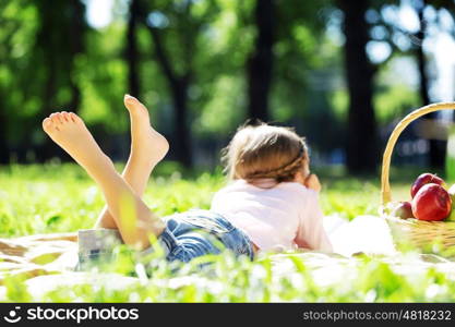 Child lying on blanket having picnic in summer park. Girl in park