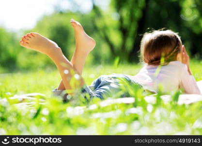 Child lying on blanket having picnic in summer park. Girl in park