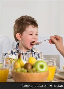 Child on breakfast - parent feeding son from spoon