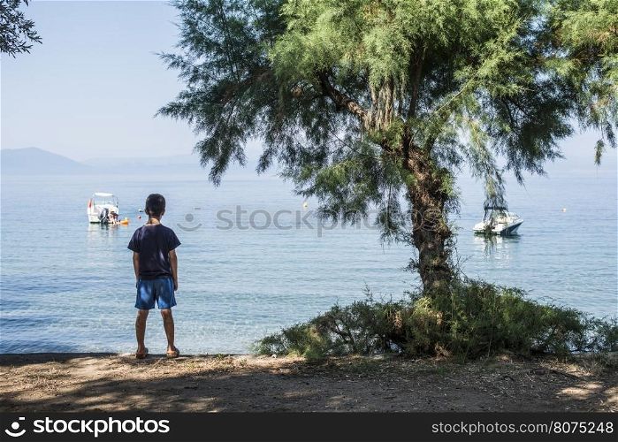 Child on the beach looking at the sea and boats.