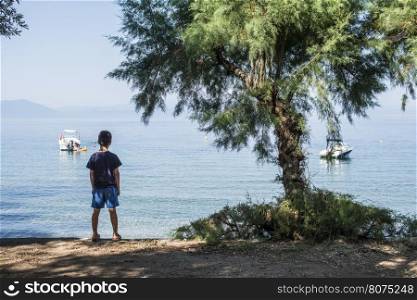 Child on the beach looking at the sea and boats.