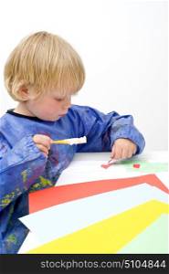 Child pasing pieces of colored paper, using a brush with glue