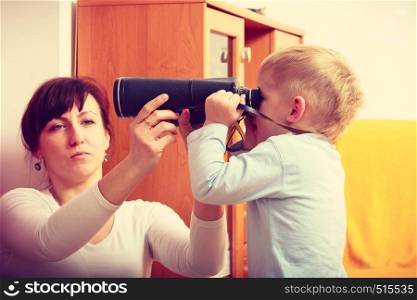 Child passion and hobbies concept. Kid playing with big professional digital camera, photographing various things in house, mother looking after him.. Kid playing with big professional digital camera