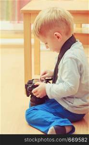 Child passion and hobbies concept. Kid playing with big professional digital camera, photographing various things in house. Kid playing with big professional digital camera