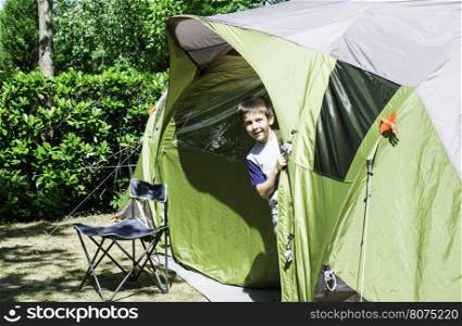 Child peeks from a green tent. Campsite