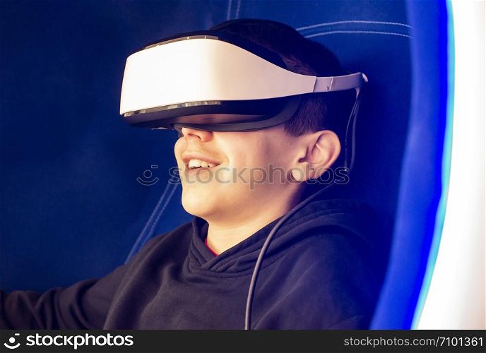 Child playing game with VR glasses. Blue illuminated cabin with joysticks. Special effects. Technology, entertainment and gaming concept with virtual reality glasses.