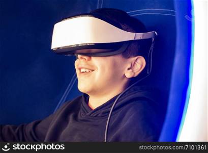 Child playing game with VR glasses. Blue illuminated cabin with joysticks. Special effects. Technology, entertainment and gaming concept with virtual reality glasses.