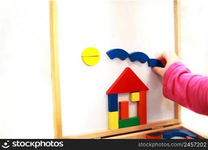 child plays wooden magnetic educational game. girl plays with a toy on a white background. child builds a house from a constructor. child plays wooden magnetic educational game. girl plays with a toy on a white background.