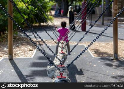 Child riding a rope snake swing in the playground at Battersea Park, London, UK