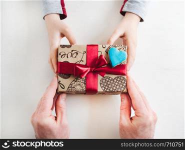 Child's hands and adult man's hands, beautiful gift box, ribbon and glazed cookies on a white, wooden background. Top view, close-up. Preparing for the holidays. Child's hands and a beautiful gift box,