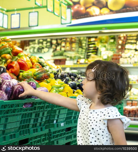 Child shopping eggplants in supermarket. Concept for buying fruits and vegetables in hypermarket. Little girl hold shopping basket.