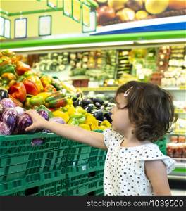 Child shopping eggplants in supermarket. Concept for buying fruits and vegetables in hypermarket. Little girl hold shopping basket.