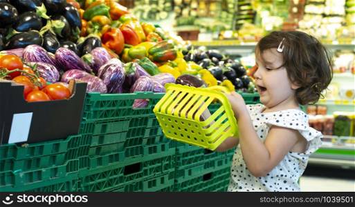 Child shopping eggplants in supermarket. Concept for buying fruits and vegetables in hypermarket. Little girl hold shopping basket.